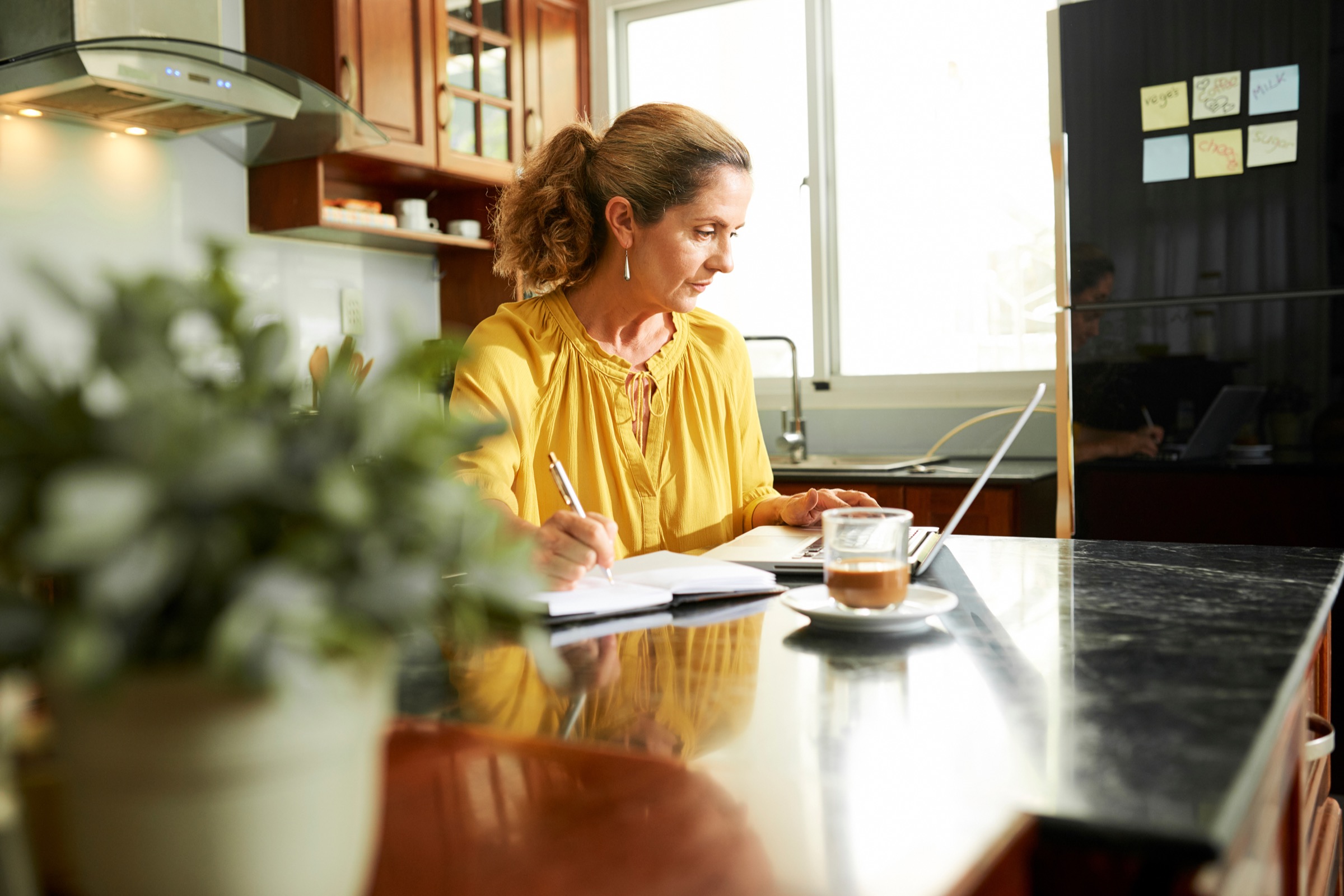 Mature woman working on laptop and taking notes